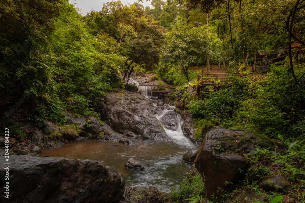 Fototapeta premium A waterfall with rocks and lush green trees in the forest.