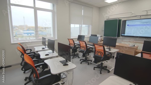 Large windows reveal outdoor landscape from empty computer classroom. Clean contemporary layout creates professional educational workspace