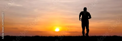 Obraz  z motywem A lone runner silhouetted against a vibrant sunset, embodying dedication and the pursuit of health. The warm hues of the sky create a dramatic backdrop for this moment of personal triumph