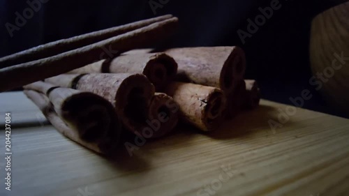 Close-up of a rustic arrangement of fragrant cinnamon sticks, scientifically known as Cinnamomum verum, resting on a natural wooden board with a blurred wooden bowl in the background. 