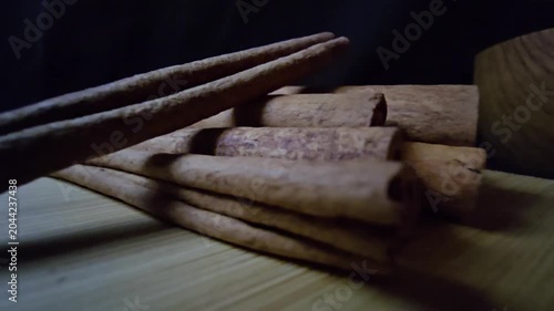 Close-up of a rustic arrangement of fragrant cinnamon sticks, scientifically known as Cinnamomum verum, resting on a natural wooden board with a blurred wooden bowl in the background. 