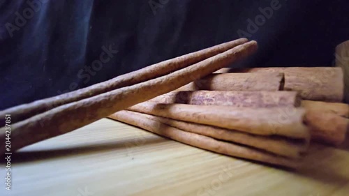 High-quality, close-up footage featuring a stack of premium Cinnamomum verum cinnamon sticks resting on a natural wooden board. The cinematic lighting emphasizes the rich, textured bark of the spice, 