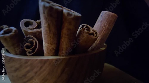 Close-up of aromatic cinnamon sticks (Cinnamomum verum) in a wooden bowl. Warm lighting highlights rich textures against a dark background. Perfect for culinary, wellness, and organic food projects.