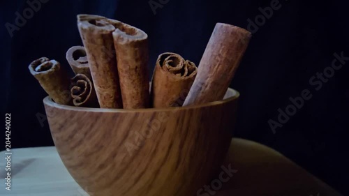 Close-up of aromatic cinnamon sticks (Cinnamomum verum) in a wooden bowl. Warm lighting highlights rich textures against a dark background. Perfect for culinary, wellness, and organic food projects.