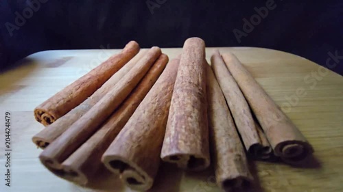 Close-up of a rustic arrangement of fragrant cinnamon sticks, scientifically known as Cinnamomum verum, resting on a natural wooden board with a blurred wooden bowl in the background. 