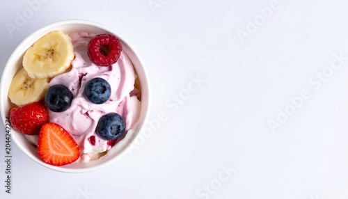 A bowl of frozen yogurt topped with fresh fruits on a bright background with wide copy space, refreshing dessert photography
