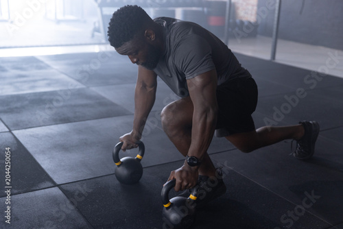 Canvastavla African American man performing kettlebell lunge on gym floor, gripping kettlebe