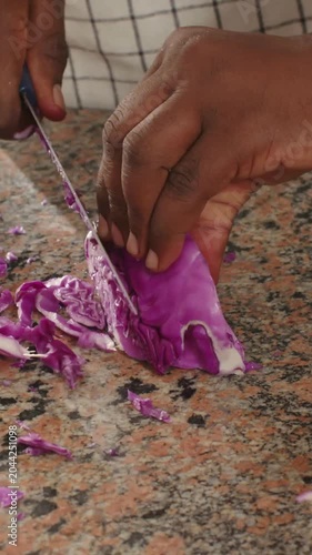 Vertical video: Placing wedge, cook hands slicing purple cabbage on counter into bowl with knife