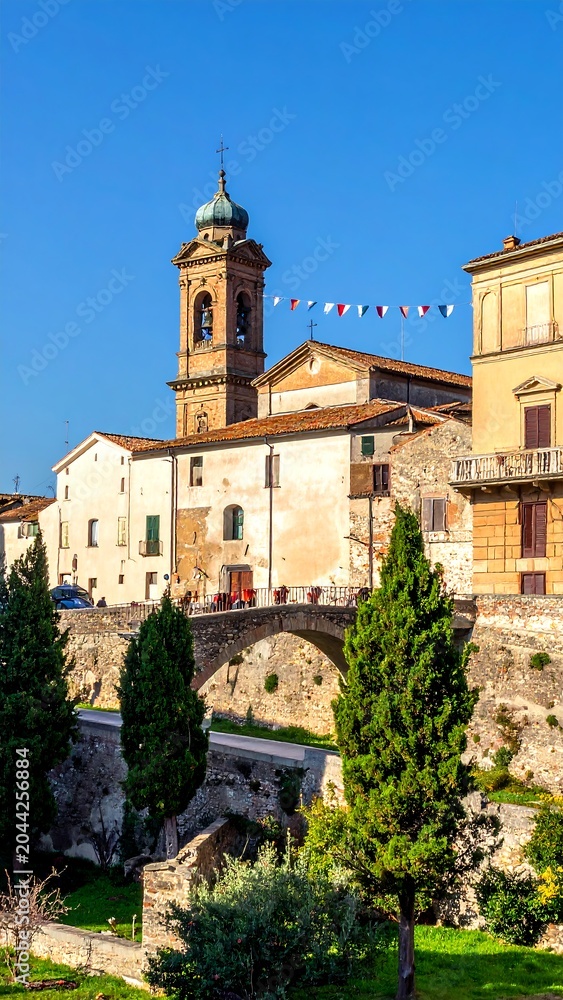 Fototapeta premium A picturesque view of an old town with a church tower, stone bridge, and lush greenery on a clear day