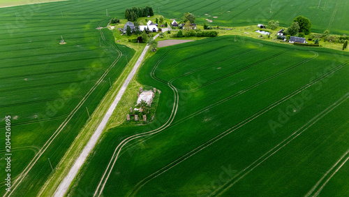 Bild auf Leinwand Beautiful aerial shot of vast green agricultural fields with a small rural village, farmhouses and old ruins