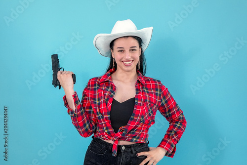 Playful young woman in cowboy hat holding toy gun indoor studio