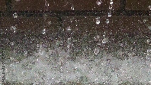水しぶきや水滴のある流れる噴水　レンガの壁を噴出される水がはじける風景　クローズアップ