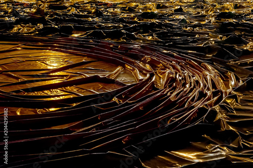 Dark, reflective material with numerous folds and wrinkles, dramatically highlighted by a warm, yellow light source