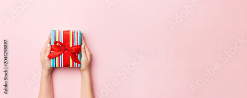 Fotografía Female's hands holding striped gift box with colored ribbon on living coral background
