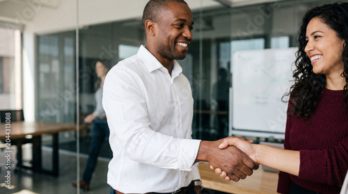 Business handshake between smiling man and woman in modern office representing partnership and professional collaboration