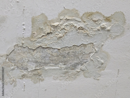 Exposed concrete cement background under peeling and cracked wall paint caused by moisture damage.