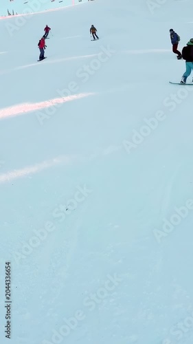 Vertical video: Lift unloading as snowboarder in pink jacket carving toward lens on slope to slow