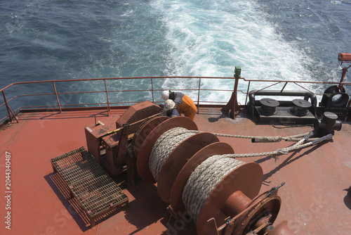 Photos crew members working on mooring winches and ropes at the stern deck of a cargo s