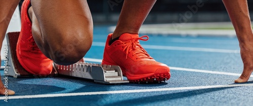 Sprinter in Bright Red Shoes at Starting Blocks on Blue Track Ready for Competition