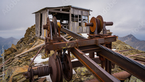 Tableau sur toile Old rusty mining machinery and a wooden shack on a rocky mountain peak with snow