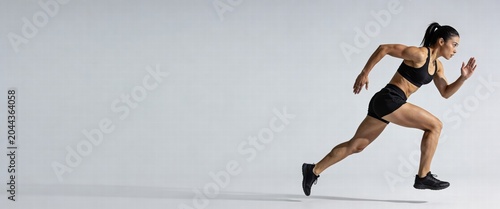 Powerful athletic woman sprinting in profile with dynamic motion on a grey studio background