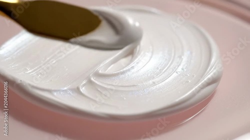 Close-up of white cream being scooped with a gold spoon from a pink dish