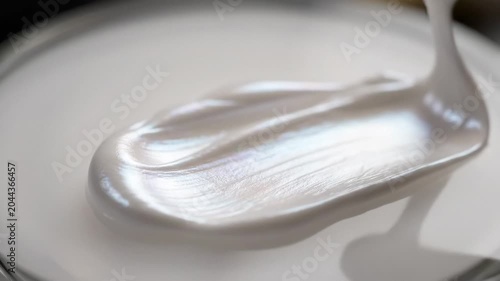 Close-up of white cosmetic cream being scooped with a spoon from a container with soft focus