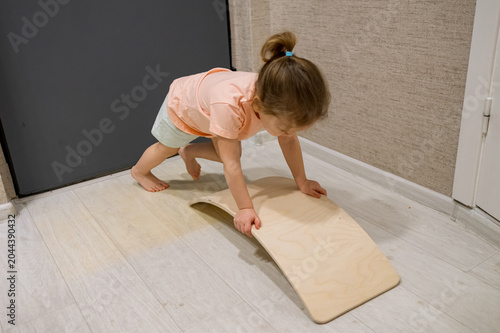 Schilderij op canvas Little child playing on a wooden balance board, crawling and carefully learning