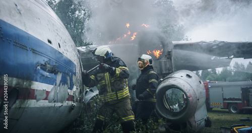 Fotografie Firefighters Pry Open a Torn Airplane Fuselage at a Smoky Forest Crash Site, Using Foam and Tools Near Active Flames as First Responders Race to Reach Survivors in a Breaking Aviation Rescue