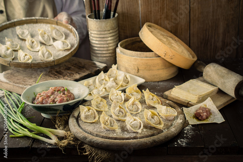 Photos An artisan chef preparing traditional Chinese wontons and dumplings with fresh minced meat, green onions, and dough on a rustic wooden table