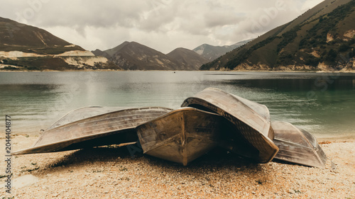 Photography several old boats on the shore of a mountain lake and high mountains and clouds