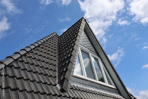 Fotografia Dark tile roof with dormer window against blue sky