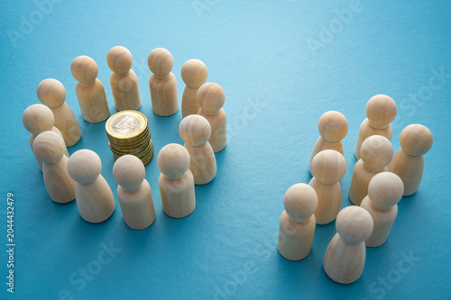 Economic inequality represented by two groups of wooden pawns: one near a pile of coins and one separated and without resources. Concepts of social exclusion, capital concentration, economic power, an