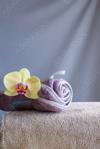 Rolled lilac towel with orchid on beige towel against gray background with copy space.