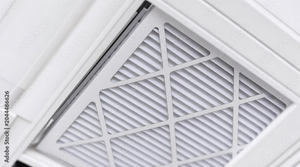 Fototapeta premium Air conditioning filter installed in a ceiling vent, showcasing a grid pattern and clean white design, part of an HVAC system in a modern indoor environment
