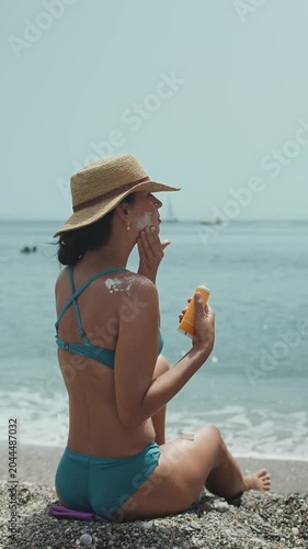 Woman applying sunscreen or sun tanning spray to her shoulder while sitting on the beach. Taking care of skin and protecting skin from the sun. Healthy holiday concept.