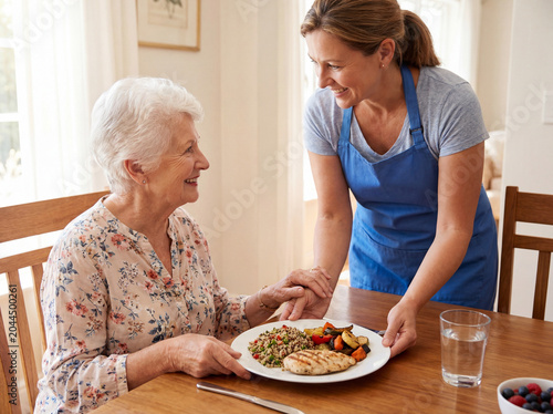 Caregiver serving healthy meal to smiling senior woman at home for nutrition and elder assistance