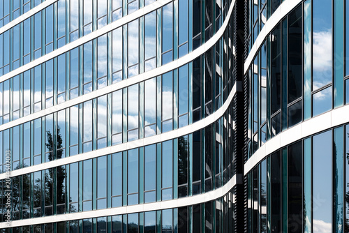 Glass facade curves across blue sky, where reflections, white bands and urban architecture form abstract office building lines in daylight
