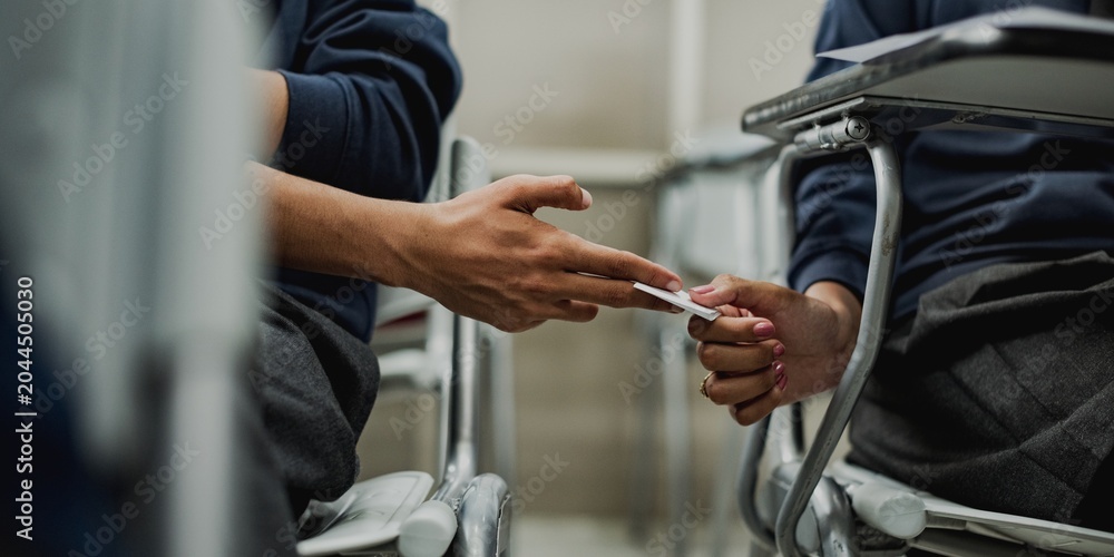 Obraz premium Two students discreetly passing a note in a classroom setting.