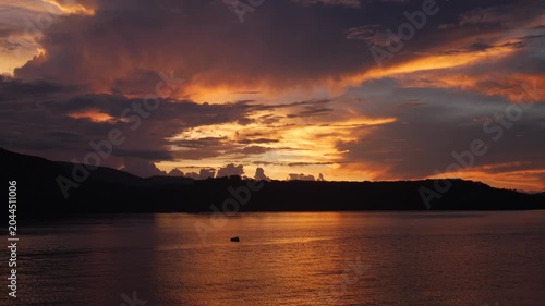Vibrant sunset over Riung Bay and the 17 Islands Marine National Park, Flores, Indonesia, with traditional boats on calm water beneath dramatic orange, gold, and purple clouds