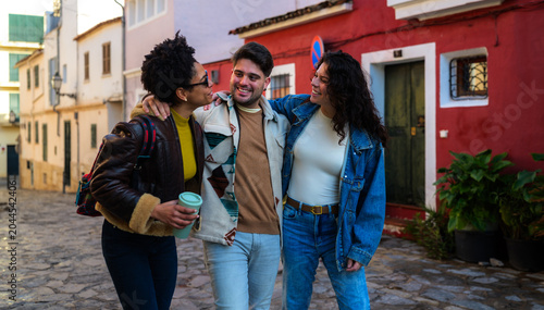 Obraz na płótnie Group of diverse friends walking on a cobblestone street, embracing each other a