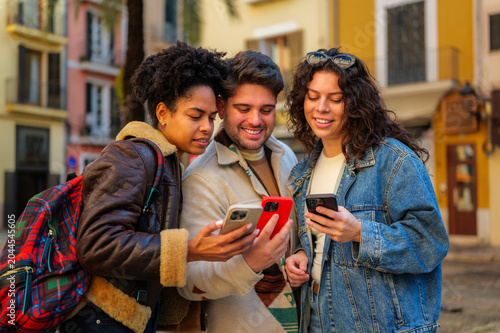 Fotografie Group of young diverse friends smiling and sharing content on their mobile phone