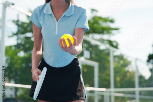 Focus on yellow ball, young caucasian woman's hand holding paddle and pickleball, preparing to serve in court on sunny day
