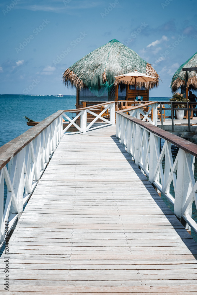 Obraz premium Luxury tropical resort vacation concept with a wooden pier extending to oceanfront overwater bungalows on a sunny summer day