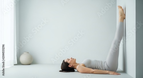 Woman performing legs up the wall pose for nervous system reset. Practicing restorative yoga against wall for body relaxation and stress relief. Mindfulness technique for mental health.