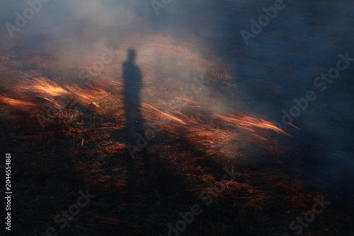 Shadow figure standing amid scorched ground with embers and smoke for dramatic apocalyptic background and poster design