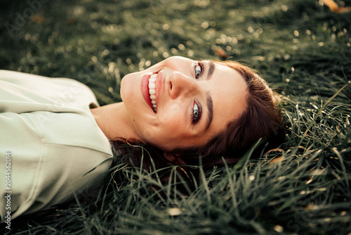 Smiling young woman lying in green grass enjoying a sunny outdoor portrait and natural happiness