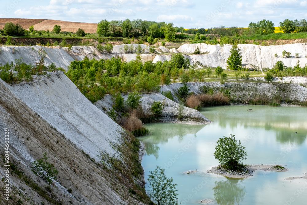 Fototapeta premium Blue quarry lake surrounded by sandy cliffs and mining landscape