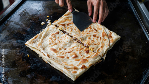 Koch bereitet knuspriges Roti Canai Fladenbrot auf Grillplatte zu