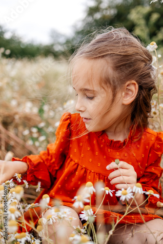 Foto Pretty 6 years old girl in orange dress is playing in the field with wild flowers